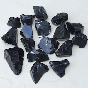 May include: A collection of black obsidian stones, each with a unique shape and texture. The stones are smooth and shiny, with a deep black color.