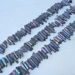 May include: A strand of iridescent black quartz crystal points, also known as black titanium quartz, arranged in rows. The crystals are faceted and have a rainbow sheen.