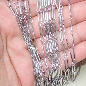 May include: Silver chain with a unique design featuring alternating small round links and longer, rectangular links.