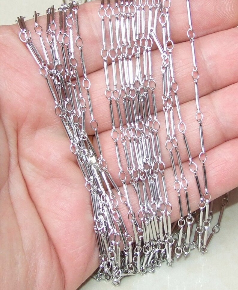 May include: Silver chain with a unique design featuring alternating small round links and longer, rectangular links.