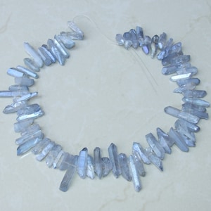May include: A strand of light blue crystal quartz points, also known as ice quartz, arranged in a circle. The points are translucent and have a slight shimmer.