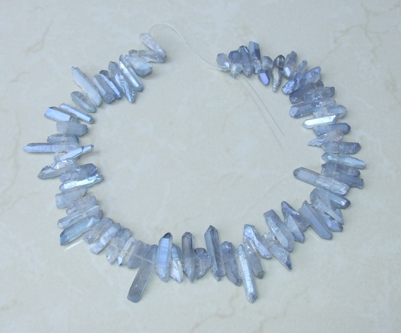 May include: A strand of light blue crystal quartz points, also known as ice quartz, arranged in a circle. The points are translucent and have a slight shimmer.