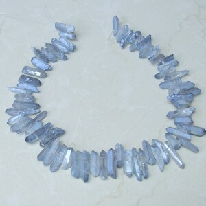 May include: A strand of light blue crystal beads, each bead is a long, thin, pointed crystal. The beads are strung on a clear thread and are arranged in a circle.