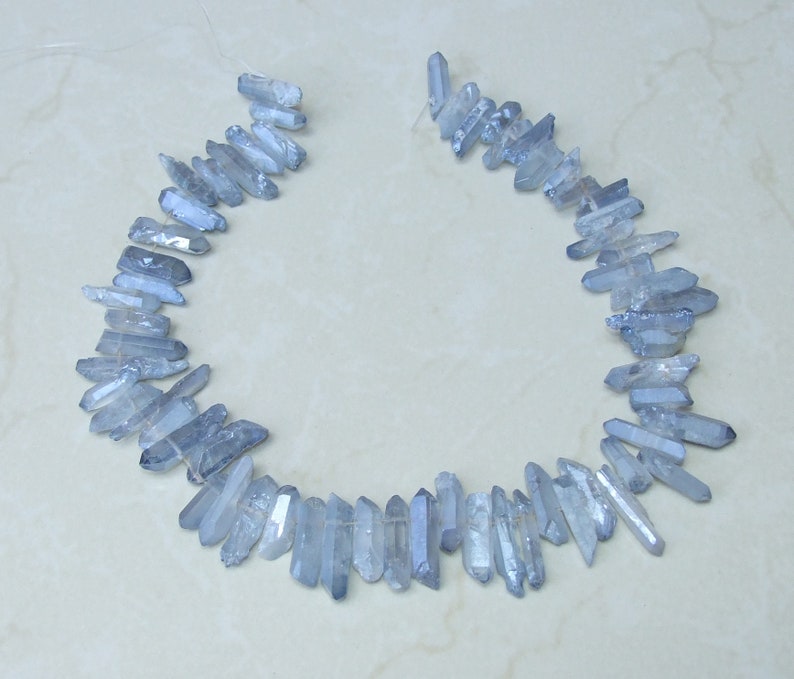 May include: A strand of light blue crystal beads, each bead is a long, thin, pointed crystal. The beads are strung on a clear thread and are arranged in a circle.