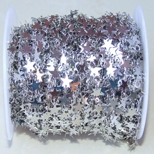 May include: A spool of silver star chain. The chain is made of small, flat, silver stars that are linked together. The chain is wound around a white spool.