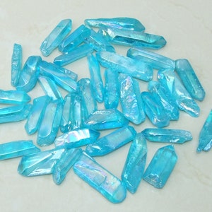 May include: A collection of approximately 30 iridescent blue crystal points. The points are all roughly the same size and shape, and they have a slightly translucent appearance.