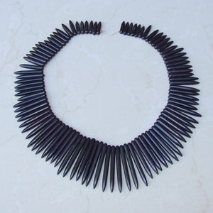 May include: A necklace made of dark purple, pointed beads. The beads are arranged in a circle, with the points facing outwards.