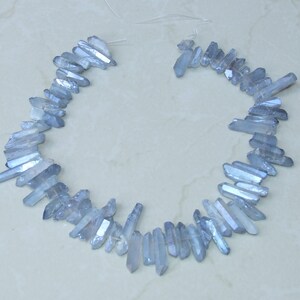 May include: A strand of light blue crystal beads, each bead is a long, thin, pointed crystal. The beads are strung together on a clear thread.