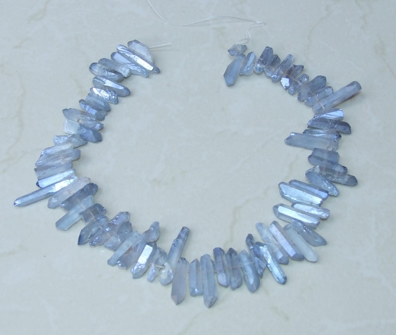 May include: A strand of light blue crystal beads, each bead is a long, thin, pointed crystal. The beads are strung together on a clear thread.
