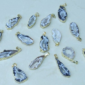 May include: A collection of 16 agate pendants with gold-plated edges. The agate is a light gray color with black veins and a hollow center. The pendants are all different shapes and sizes.
