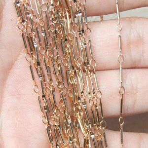 May include: Gold chain with a rectangular link design. The chain is made of multiple strands and is shown in a hand.
