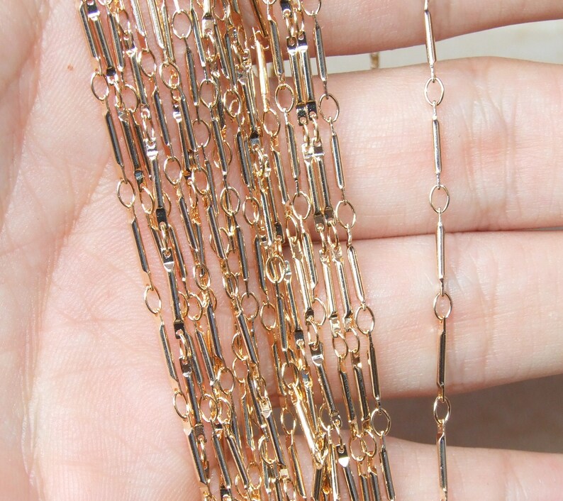 May include: Gold chain with a rectangular link design. The chain is made of multiple strands and is shown in a hand.