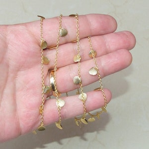 May include: A gold chain necklace with small, gold, shell-shaped charms. The necklace is on a hand, and the charms are dangling.