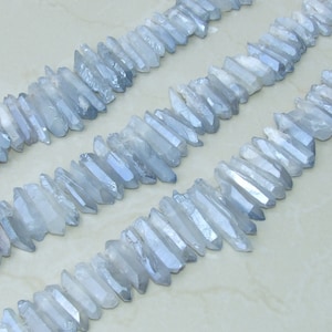 May include: A strand of light blue crystal points, also known as quartz points, arranged in rows. The points are faceted and have a shimmery, iridescent finish.