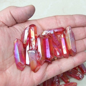 May include: A collection of red iridescent quartz points, also known as aura quartz, in various sizes. The points are translucent and have a metallic sheen.