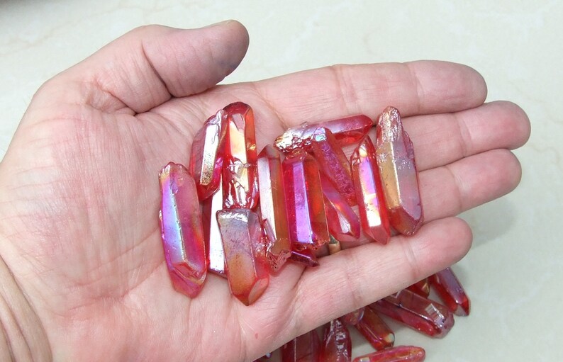 May include: A collection of red iridescent quartz points, also known as aura quartz, in various sizes. The points are translucent and have a metallic sheen.