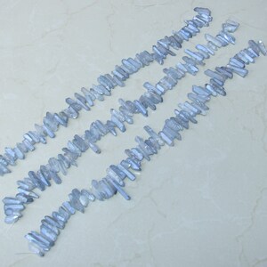 May include: A strand of light blue crystal beads, each bead is a long, thin, pointed crystal. The beads are arranged in rows, with the points of the crystals facing the same direction.