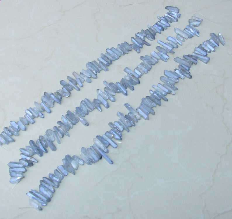 May include: A strand of light blue crystal beads, each bead is a long, thin, pointed crystal. The beads are arranged in rows, with the points of the crystals facing the same direction.