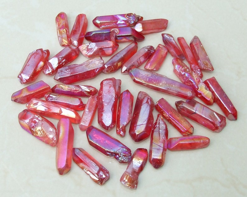 May include: A collection of approximately 30 red iridescent quartz points. The points are various sizes and shapes, with a natural, raw finish.
