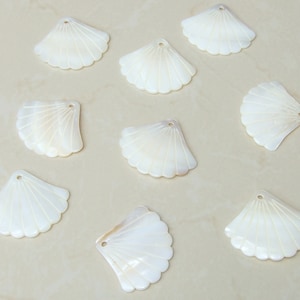 May include: Ten white seashell-shaped decorative pieces with a fan-like pattern. The shells are smooth and have a pearly sheen.