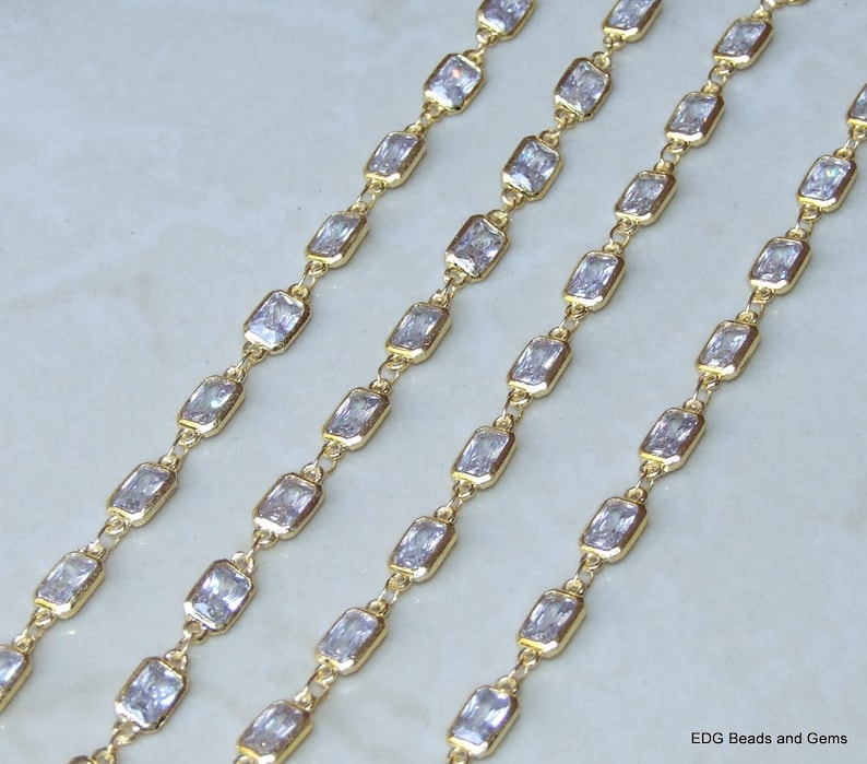 Op de afbeelding: Vier strengen gouden ketting met heldere rechthoekige zirkonia-stenen. De ketting is gemaakt van kleine, met elkaar verbonden metalen stukken.