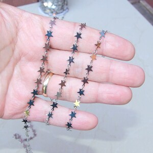 May include: A silver chain with small star-shaped links. The chain is coiled in a hand.