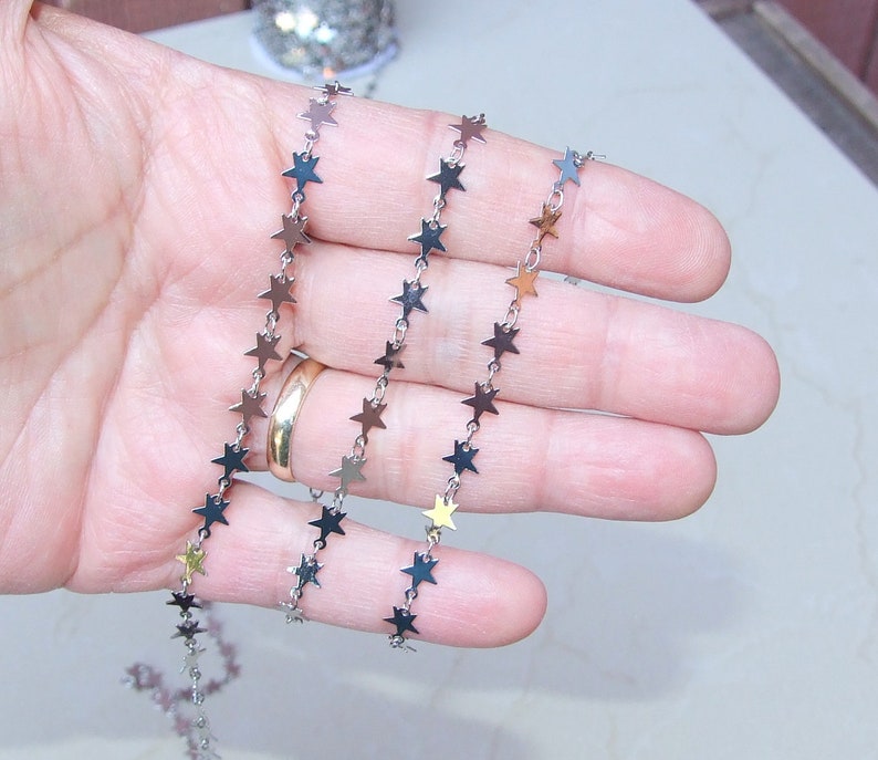 May include: A silver chain with small star-shaped links. The chain is coiled in a hand.