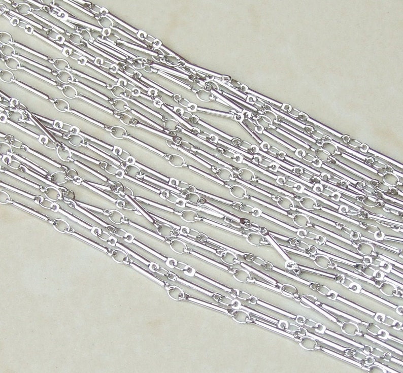 May include: Silver chain with alternating long and short links. The chain is made of metal and has a polished finish.