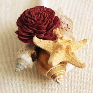 May include: A burgundy flower with a white lace accent, surrounded by seashells and a starfish.