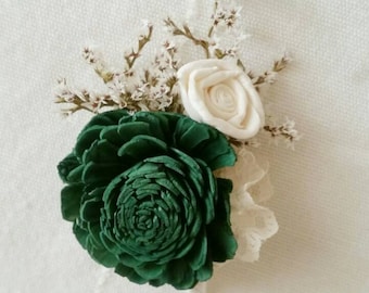May include: A green and white sola wood flower boutonniere with a white lace accent. The boutonniere is perfect for a wedding or special occasion.