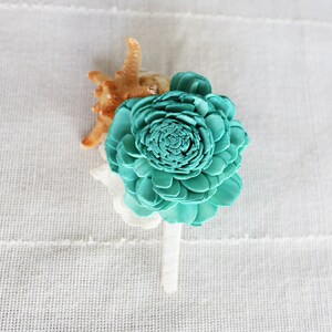 May include: A teal blue sola wood flower with a seashell accent. The flower is attached to a white stem.