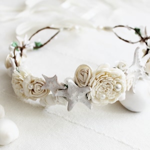 May include: A white floral crown with starfish and seashells. The crown is made of twigs and white flowers with pearl accents.