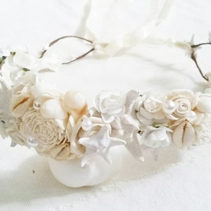 May include: A white floral crown with seashells and pearls. The crown is made with white flowers, seashells, and pearls. It is a beautiful and delicate piece of jewelry.