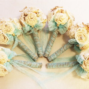 May include: Six ivory and beige flower bouquets with seashells and lace accents. The bouquets have a rustic burlap and lace wrap with a light blue ribbon.