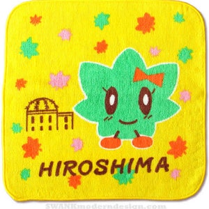 May include: A yellow hand towel with a green cartoon character with a red bow and the word "HIROSHIMA" in brown letters. The character is surrounded by small red, pink, and green leaves.