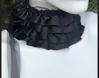 May include: A black satin choker with multiple ruffles and a black tulle bow. The choker is adorned with small black beads.