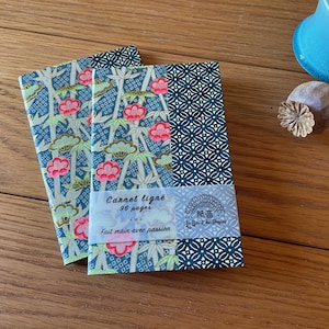May include: Two notebooks with floral and geometric patterns. The covers feature a blue background with pink flowers and green foliage. The notebooks are labelled "Carnet ligné 96 pages" and "Fait main avec passion".