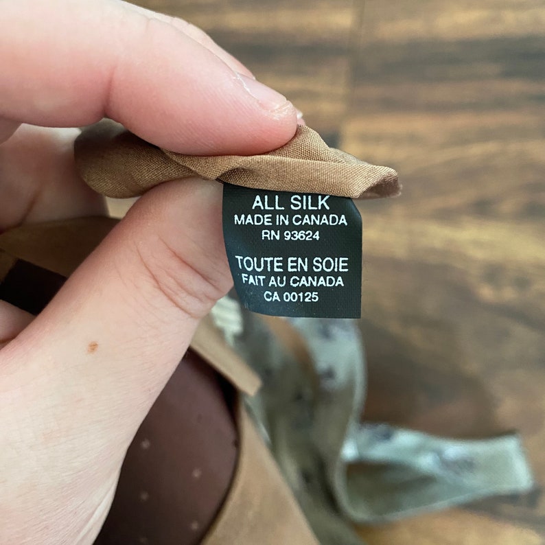 May include: A brown fabric label with black text that reads "ALL SILK MADE IN CANADA RN 93624 TOUTE EN SOIE FAIT AU CANADA CA 00125".