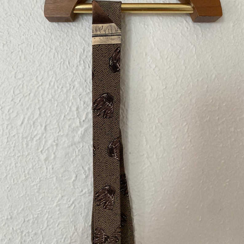 May include: A brown patterned tie with a brown and white geometric design. The tie is hanging on a wooden hanger.