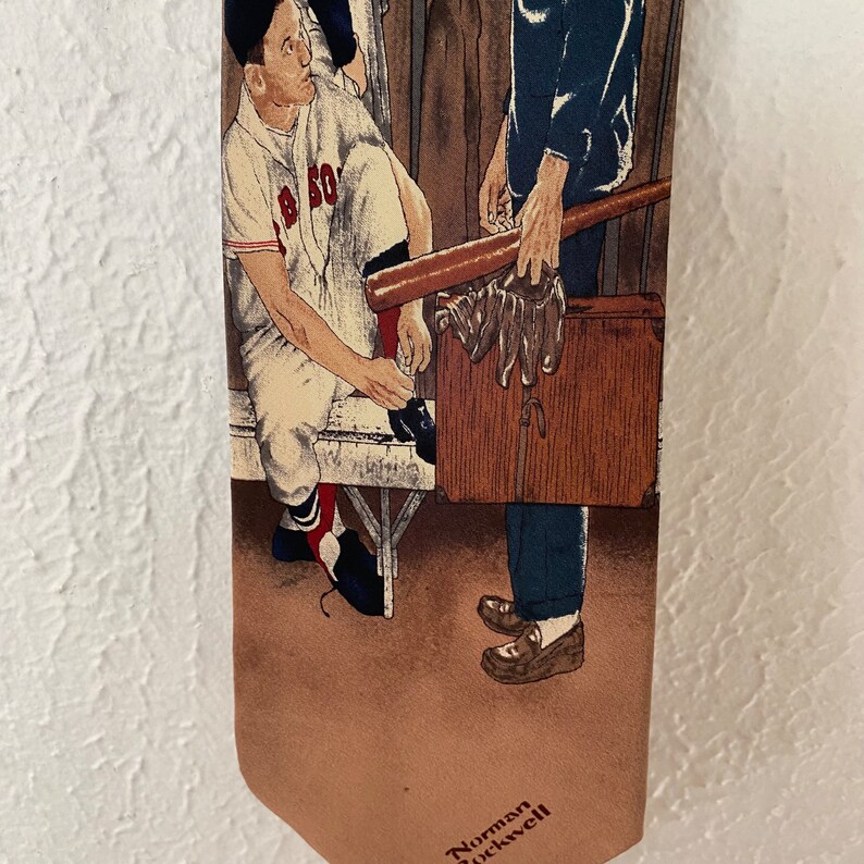 May include: A brown and tan tie with a baseball scene. A man in a baseball uniform is holding a bat and looking at a man in a suit. The text "Norman Rockwell" is at the bottom of the tie.
