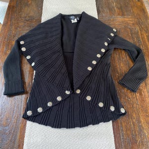 May include: Black knitted cardigan with a draped collar and silver button accents.