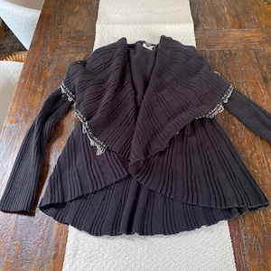 May include: Black knitted cardigan with a draped front and silver chain detailing on the sleeves.