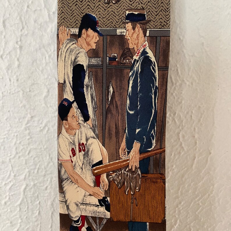 May include: A vintage tie featuring a colorful illustration of three baseball players in a locker room. The players are wearing baseball uniforms and holding bats. The tie is made of a woven fabric and has a brown background.