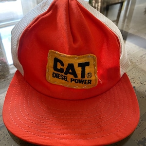 May include: A red and white trucker hat with a yellow patch that says "CAT DIESEL POWER" in black lettering.