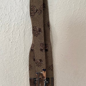 May include: A brown patterned tie with a brown and white chevron pattern. The tie features a repeated image of a baseball glove and a baseball player.