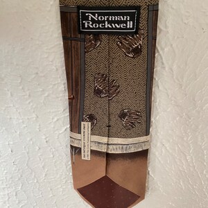 May include: A brown silk tie with a pattern of brown mittens and a brown wooden door. The tie has a brown label with the text "Norman Rockwell" and "The Saturday Evening Post 1960 The Curtis Publishing Company".