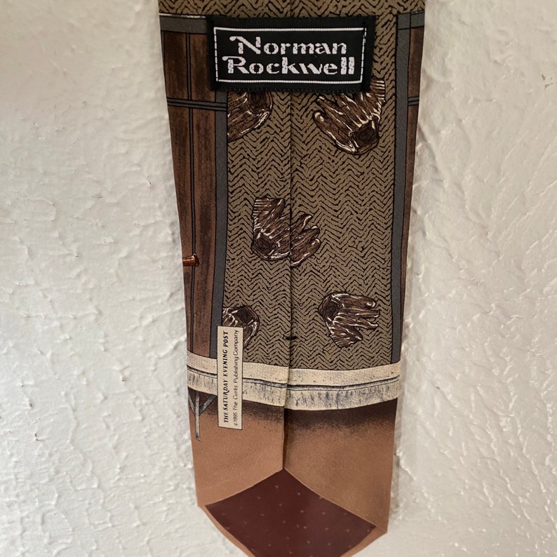 May include: A brown silk tie with a pattern of brown mittens and a brown wooden door. The tie has a brown label with the text "Norman Rockwell" and "The Saturday Evening Post 1960 The Curtis Publishing Company".