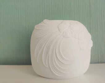 May include: White ceramic vase with a raised floral design. The vase has a smooth, matte finish and a rounded shape.