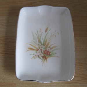 May include: White rectangular ceramic dish with a gold rim. The dish features a floral design with wheat stalks, white daisies, and red flowers.