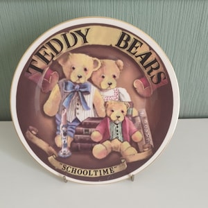 May include: A decorative ceramic plate featuring three teddy bears dressed in school uniforms. The plate has a brown background with gold trim and the words "Teddy Bears" and "Schooltime" written on it.